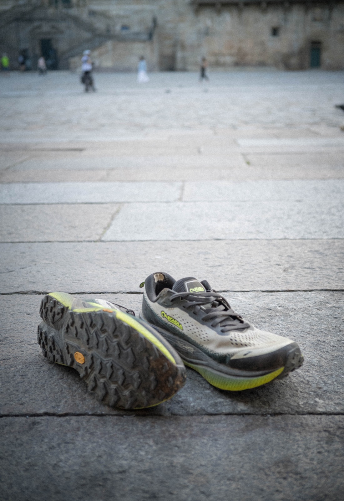 The Brooks Cascadia 20s, trail dirt still caked in the lugs, resting on the granite of Praza do Obradoiro in front of the Santiago cathedral.