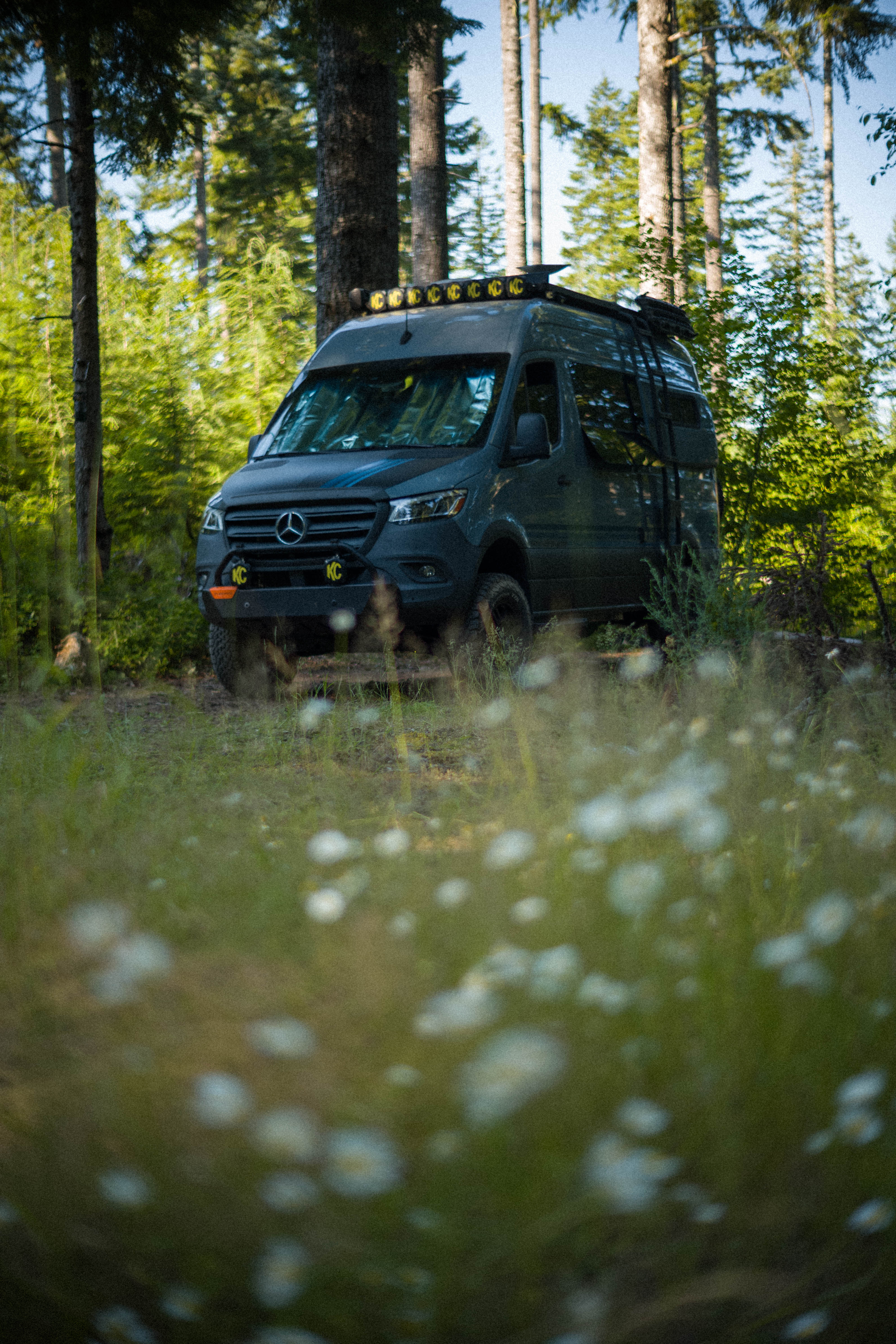 My van at dusk with the KC light bar on, parked at a forest campsite